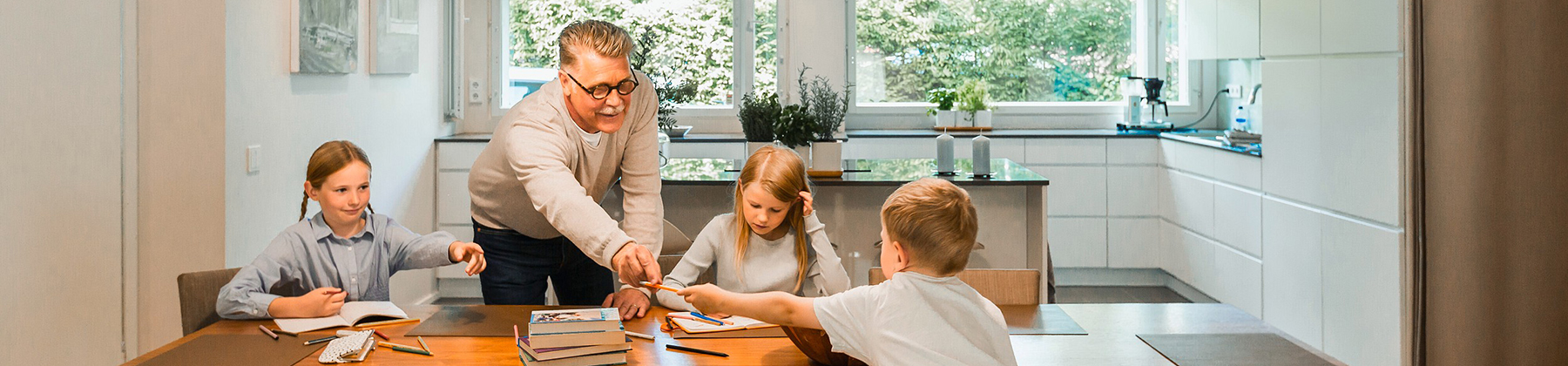 Lapset tekevät läksyjä ruokapöydän ääressä. Isovanhempi ojentaa lapselle kynän.