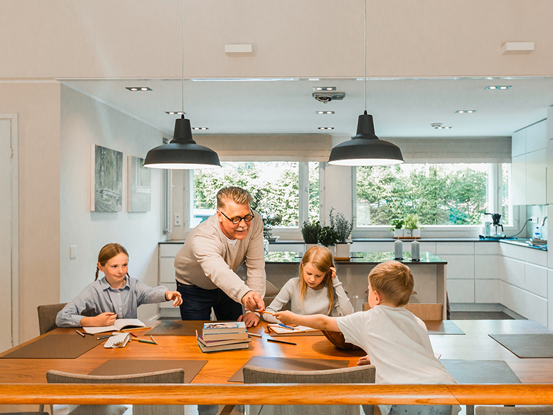 Children doing homework at the dining table while a grandparent hands a pencil to a child