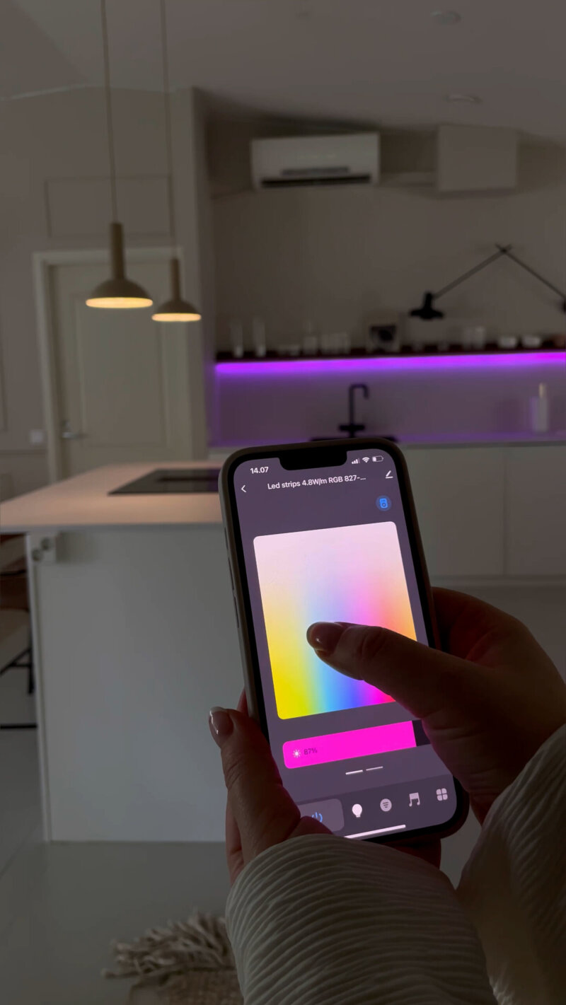 Keittiön saarekkeen yllä kaksi riippuvalaisinta, molempien valoa säädetään parhaillaan Airam SmartHome -sovelluksella. Taustalla hylly, jonka alle on kiinnitetty Airam SmartHome -lednauha, jonka sävyä säädetään juuri violetiksi.