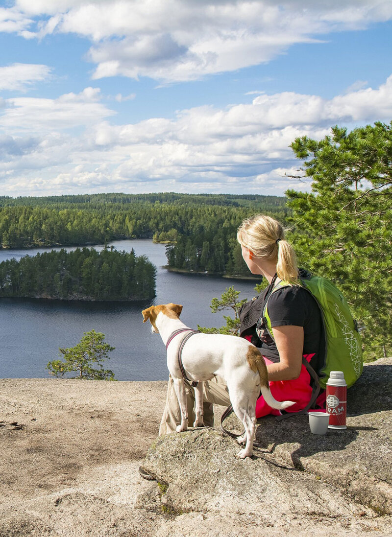 Mallinnuskuva. Nainen istuu koiran kanssa kansallismaisemassa. Mukana on Airam Klassikko-termospullo